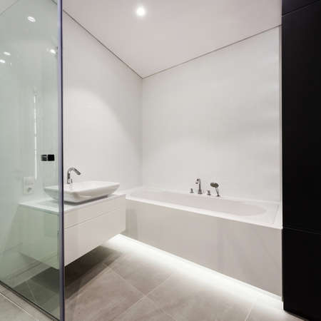 Side view element of modern house with glass door at contemporary interior design in bathroom, white bath, sink on countertop against empty copy space wallの写真素材