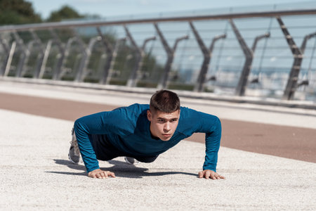 Serious and motivated young sportsman making sport training outdoors alone, doing push ups exercise...