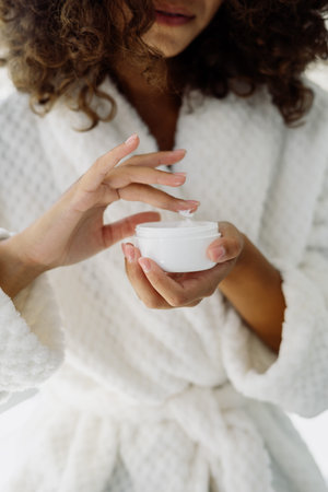 Concept of beauty procedure. Vertical cropped view of afro american woman holding cream in hands,...