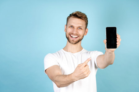 Selective focus on modern smartphone with blank screen display. Happy adult guy in white t-shirt...