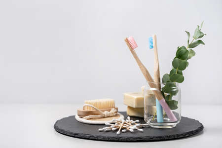 Zero waste concept. Bamboo toothbrush in cup, nail brush, organic solid soap, wooden ear sticks and all bathroom supplies with eucalyptus plant on black plate stand against white copy space backgroundの写真素材