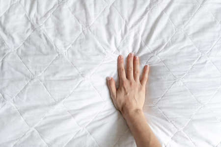 Top view of woman hand testing white orthopedic mattress on firmness. Cropped view of female pressing hypoallergenic foam surface to check its softness at copy space backgroundの写真素材