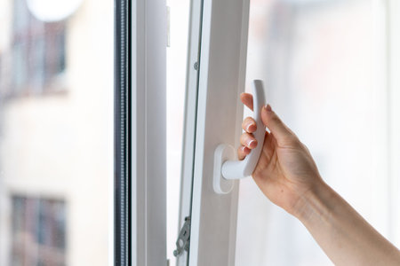 Cropped view of woman holding white modern handle at pvc window with double glazing, opening plastic...
