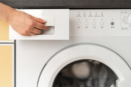 Cropped view of woman hand opened detergent box at new modern washing machine. Housewife doing...