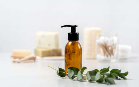 Concept of biodegradable cosmetics. Selective focus on glass dispenser bottle with natural soap, organic shower gel and shampoo near eucalyptus plant against blurred copy space backgroundの写真素材