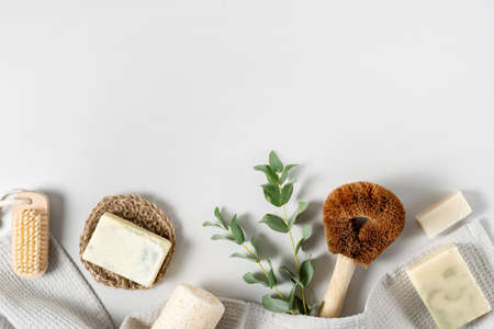 Concept of ecological and recycled objects. Flat lay, top view of natural, organic items for home, coconut brush, luffa sponge, solid soap, towel and eucalyptus plant on white copy space backgroundの写真素材