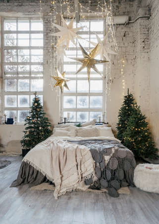 Vertical photo of beautiful cozy bedroom with winter style interior, decoration new year tree, garland lights, comfort bed and traditional holiday decor at home with copy spaceの写真素材