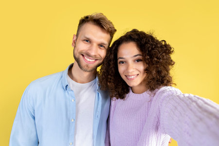 Young afro american woman and smiling man standing together on yellow background with copy space,...