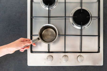 Top view of woman hand holding pan on modern kitchen gas stove cooker with burner. Housewife cooking food, boiled water and using metal kitchenwareの写真素材