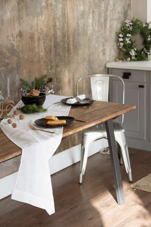 Concept of holiday breakfast. Vertical view of cozy kitchen in loft style interior with tablecloth, served plates and home decor on dining table near copy space wall, against cupboards furnitureの写真素材