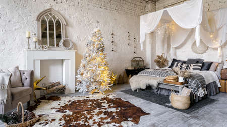 Panoramic view of cozy bedroom with loft interior design, white decorative fireplace, armchair and christmas tree near comfort bed. Home decor and winter or new year decoration in roomの写真素材