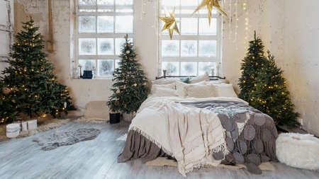 Panoramic view of beautiful cozy bedroom with winter style interior, decorated new year tree, garland lights, comfort bed, present boxes and traditional decor at homeの写真素材