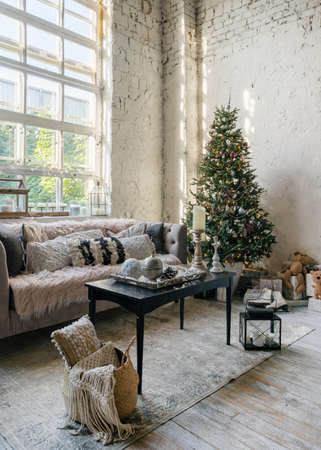 Vertical photo of cozy living room with soft cushions on comfortable couch and new year decoration at christmas tree. Modern apartment with loft interior designの写真素材