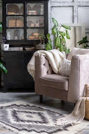 Vertical photo of black vintage chest of drawers near comfortable armchair with cozy plaid and cushions. Living room with furniture in house with ethnic carpet and modern interior designの写真素材