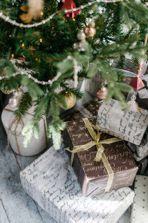 Vertical photo of new year present boxes under decorated christmas tree. Element of cozy interior with simple and craft package. Concept of preparation for december holidaysの写真素材