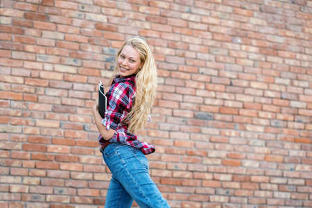 Concept of graduation and successful education. Side view of happy and joyful academy student girl jumping with copybooks after exams on courses or faculty against brick copy space wall on backgroundの写真素材