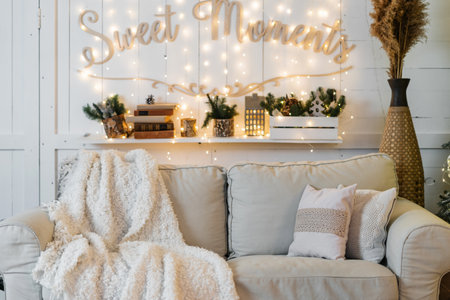 Comfortable living room with white and soft couch, house decor and evergreen plants in flowerpots near garland light. Elements of interior in boho chic styleの写真素材
