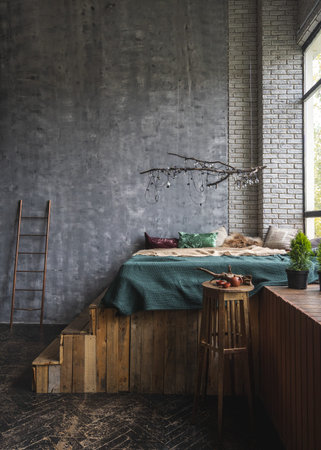 Vertical view of light bulb garland on wooden branch over comfort bed, against grey copy space wall....