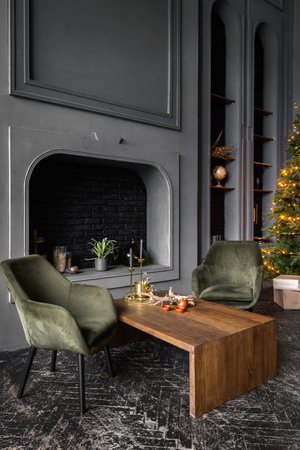 Vertical view of classic living room with comfort armchairs near wooden table against decorative fireplace, home decor and new year tree and christmas presents in loft style apartmentの写真素材