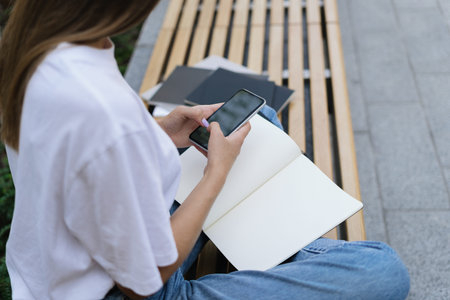 Cropped side view of adult academy student girl using online app on smartphone, resting after...