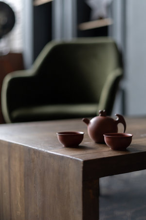 Selective focus on ceramic teapot with hot tea beverage. Vertical view of chinese ceremony in living room with classic design against blurred background. Concept of still life in dark interiorの写真素材