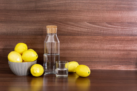 Wellness and detox concept. Bowl with fresh juicy lemons lying near crystal and pure water in glass bottle. Wooden countertop at kitchen with copy spaceの写真素材