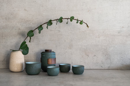 Set for chinese tea ceremony standing near branch in vase at marble countertop on modern kitchen. Still life concept. Small cups, kettle and plant against copy space wallの写真素材