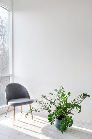 Vertical view of grey comfortable armchair standing on wooden floor near window and green houseplant. Elements of living room with modern furnishing and home decorの写真素材