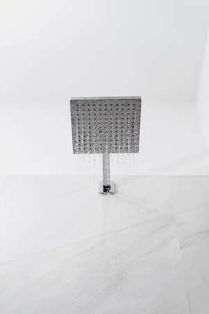 Vertical view of ceiling shower head with water drops in white modern bathroom. Contemporary and minimalist home interior with chrome plumbing elementの写真素材