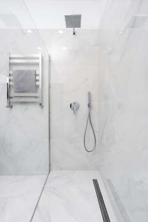 Vertical view of contemporary bathroom interior with glass wall in shower cabin, towel on heated rail and plumbing elements at white ceramic tiled wallの写真素材