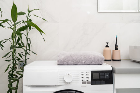 Clean and fresh towels on automatic washing machine near bathroom cupboard with electric toothbrush,...