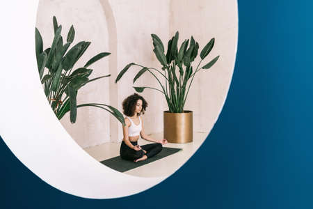 Peaceful and tranquil african american yogi in deep meditation doing breathing exercise. Calm woman training at yoga studio, sitting on fitness mat. Self healing and mental health conceptの写真素材