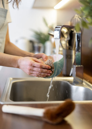Household and eco friendly supplies concept. Vertical view of woman standing on kitchen, washing...