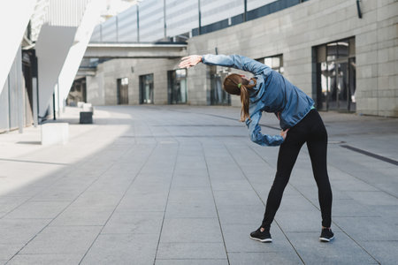 Back view of young adult athlete woman in sportswear stretching body before cardio workout, spending...