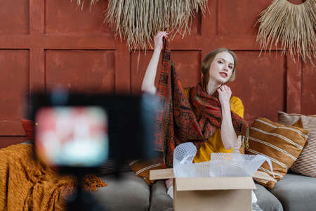 Young adult online shopper and blogger creating media content for internet blog, recording video at broadcasting equipment, showing purchaseの写真素材