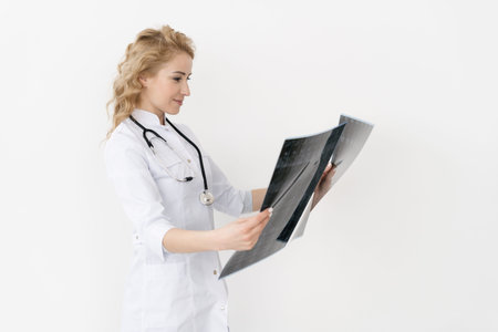 Qualified woman doctor in white uniform checking x-ray film, diagnose patient injury, smiling calm and standing isolated on studio background with copy space. Healthcare and medical insurance conceptの写真素材