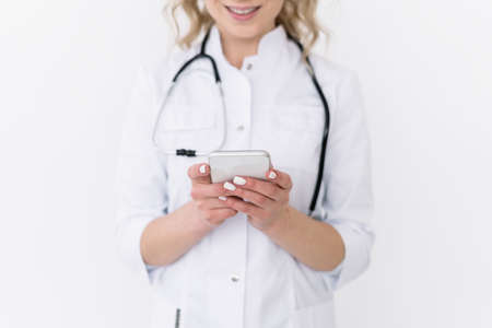 Cropped view of family doctor in white coat hold modern smartphone in hands, consult patient online. General practitioner use cellphone device, text message to client. Medicine technology conceptの写真素材