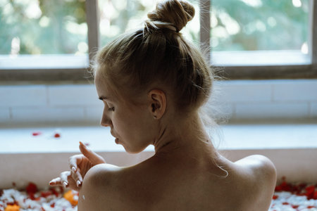Body care concept. Back view of calm and dreamy young adult woman taking bath with tropical flowers,...