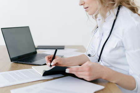 Concept of treatment plan and patient health report. Cropped view of doctor write medical history or anamnesis in journal. Nurse work at private clinic, noted information in notepadの写真素材