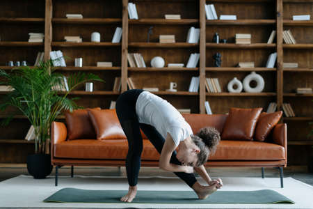 Sporty afro american woman stretching legs, doing sport training on exercise mat. Young female wear sportswear, make workout in living room at home. Leisure and lifestyle conceptの写真素材