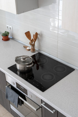 High angle view of black ceramic induction stove with saucepan on clean surface. Contemporary home...