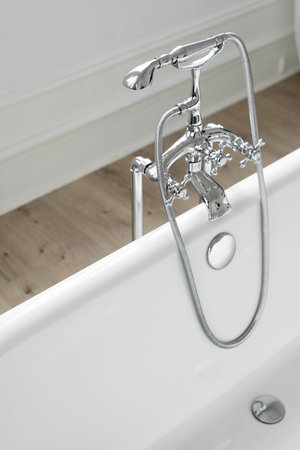 Silver shower head and faucet over white empty bathtub. Classic bath with chrome water tap in modern...