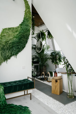 Vertical shot of bathroom with green houseplants and sofa in relax area. Apartment with cozy interior design in boho style decorated tropical plants. Bohemian room with natural wooden and wicker decorの写真素材