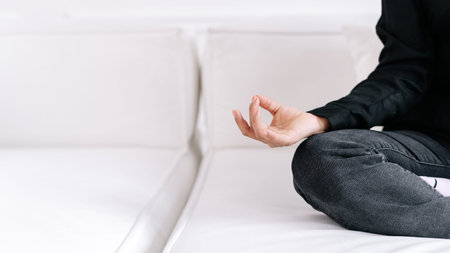 Cropped shot of calm peaceful young woman sitting in lotus asana on white couch, showing shuni mudra...
