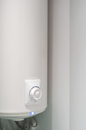 Vertical shot of white bathroom boiler with control knob and light indicator hanging on wall. Water heating in modern houseの写真素材