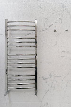 Vertical shot of shiny straight chrome heated radiator in simple design with coated towel rails mounted on modern bathroom gray marble tile wallの写真素材