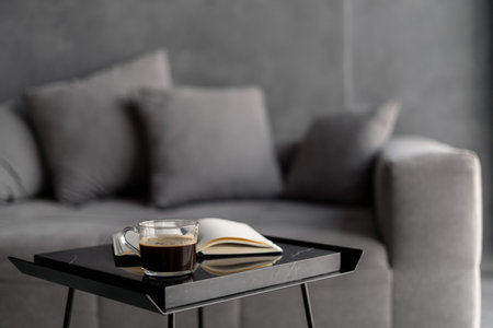Selective focus on table with cup of coffee and open book against blurred background. Comfortable...