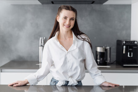Young happy woman standing behind countertop, preparing to cooking alone in modern kitchen interior,...