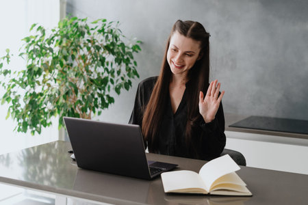 Remote work concept. Happy young businesswoman sitting behind table in home office, looking at...