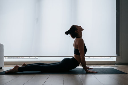 Silhouette of attractive slim woman doing exercise on yoga mat at home, warming up her body muscles before workout indoors. Healthy lifestyle, fitness and sport conceptの写真素材